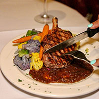 Someone cutting a porkchop on a plate with vegetable sides