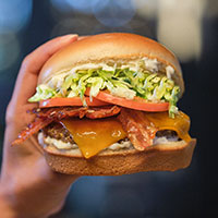 Burger with bacon, cheese, lettuce and tomatoes in someone's hand