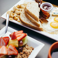 A plate with Eggs, bacon, slices of bread, potatoes. A second plate with fruits and nuts